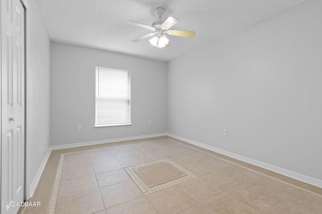 empty room with ceiling fan, a textured ceiling, and light tile patterned floors