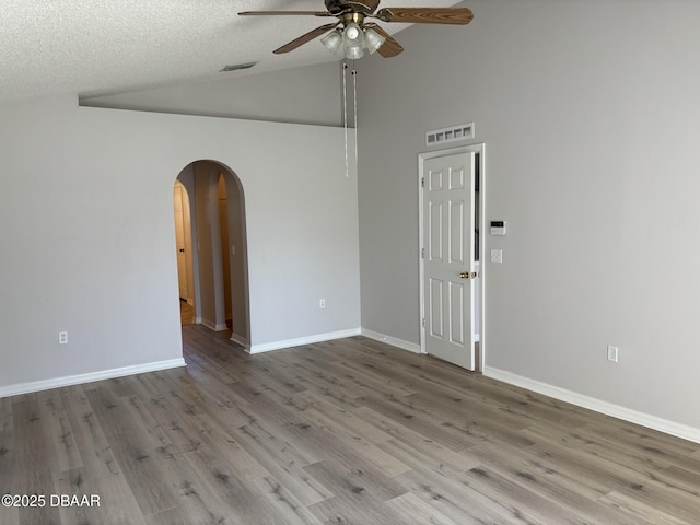 empty room featuring arched walkways, lofted ceiling, visible vents, light wood-style flooring, and ceiling fan