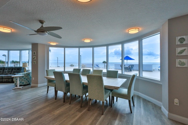 dining area with a textured ceiling, hardwood / wood-style floors, a water view, and ceiling fan