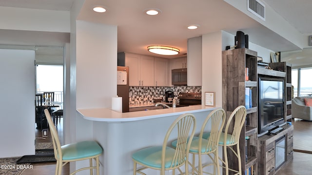 kitchen with wood-type flooring, decorative backsplash, kitchen peninsula, black appliances, and a breakfast bar