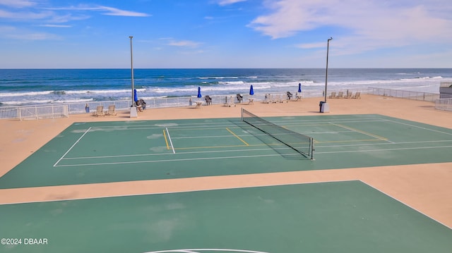 view of tennis court with a water view and a view of the beach