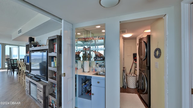 interior space with stacked washer / dryer, sink, light wood-type flooring, and black fridge