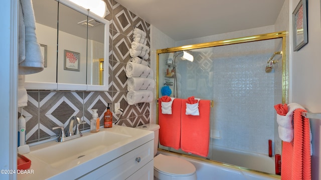 full bathroom with tile walls, shower / bath combination with glass door, vanity, toilet, and decorative backsplash