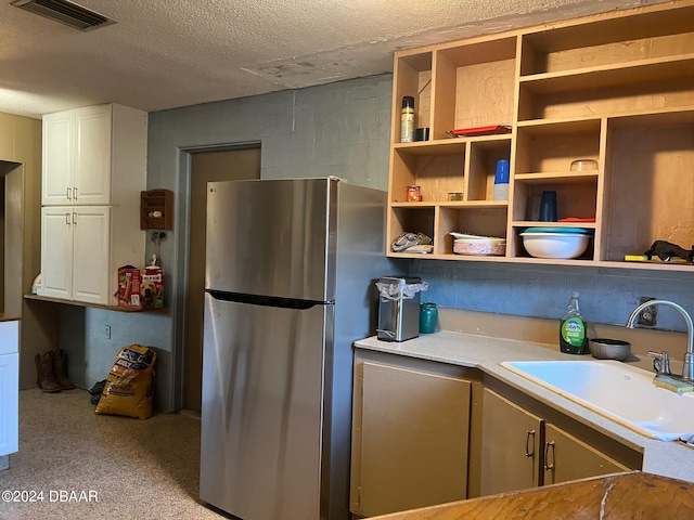 kitchen featuring white cabinetry, sink, stainless steel fridge, and a textured ceiling