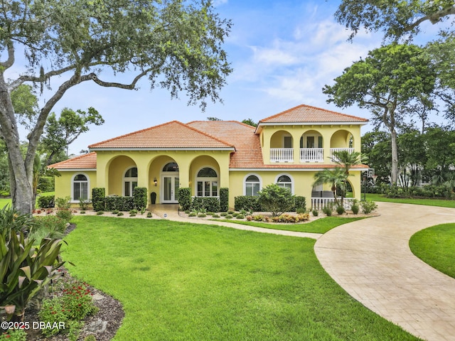 1207 Kaleen Dr, Ormond Beach, FL 32174 - mediterranean / spanish-style home featuring curved driveway, stucco siding, a front lawn, a balcony, and a tiled roof