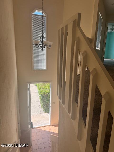 stairway with a high ceiling, tile patterned floors, and an inviting chandelier