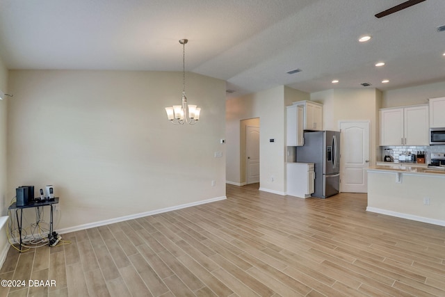 kitchen with lofted ceiling, an inviting chandelier, light hardwood / wood-style flooring, white cabinetry, and appliances with stainless steel finishes