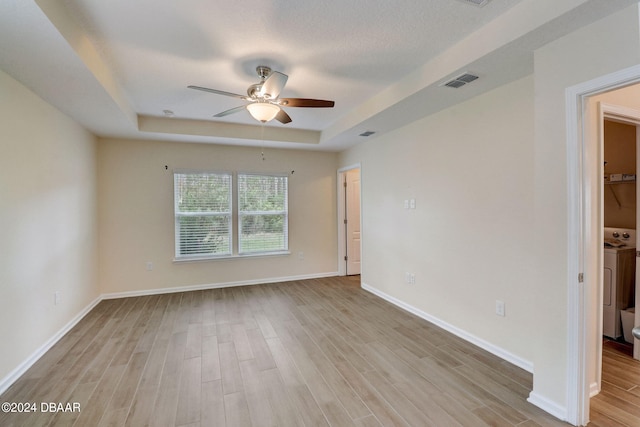 unfurnished room with light hardwood / wood-style floors, ceiling fan, washer and clothes dryer, and a tray ceiling