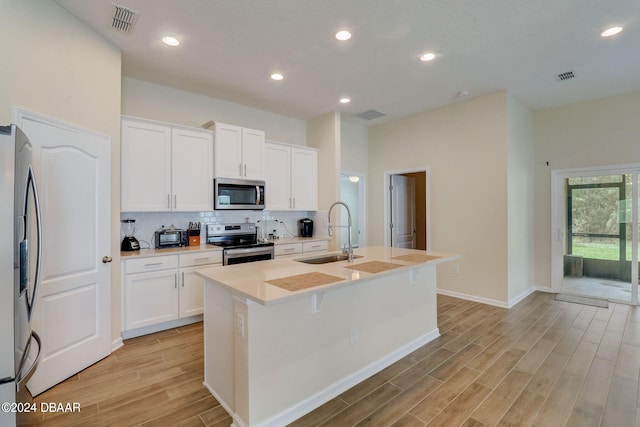 kitchen with a center island with sink, sink, white cabinetry, appliances with stainless steel finishes, and light hardwood / wood-style flooring