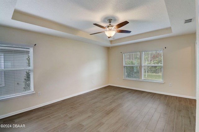 unfurnished room with light hardwood / wood-style flooring, ceiling fan, and a raised ceiling