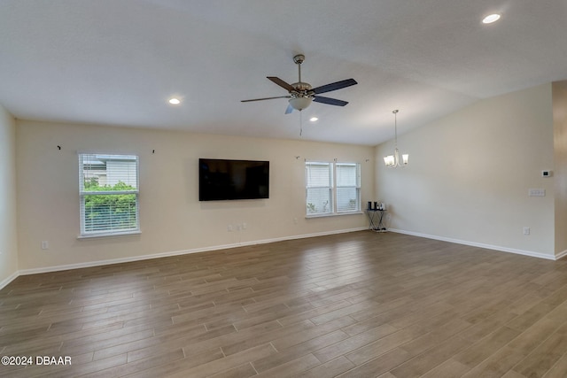 unfurnished living room with light hardwood / wood-style floors, ceiling fan with notable chandelier, plenty of natural light, and vaulted ceiling