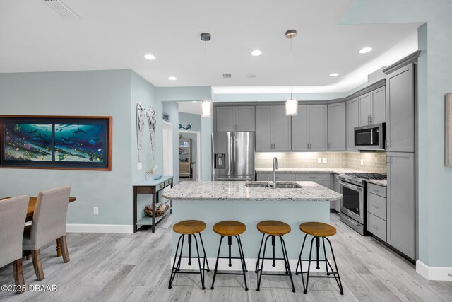 308 Low Tide Ln, Daytona Beach, FL 32124 - kitchen with appliances with stainless steel finishes, gray cabinetry, light wood-style flooring, a kitchen island with sink, and tasteful backsplash