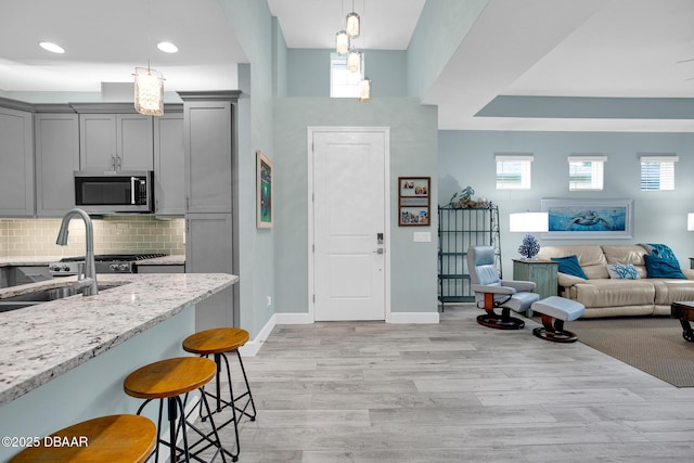 308 Low Tide Ln, Daytona Beach, FL 32124 - kitchen with stainless steel microwave, gray cabinets, a kitchen breakfast bar, light stone counters, and light wood-type flooring