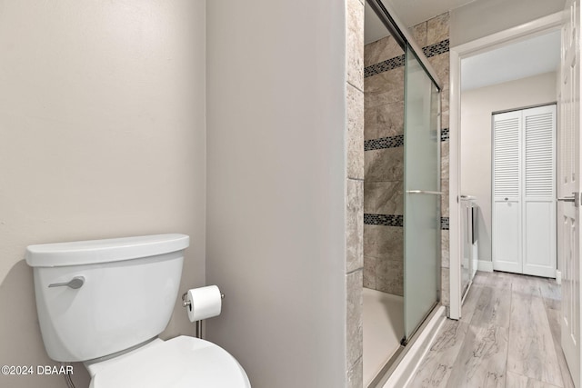 bathroom with hardwood / wood-style floors, a shower with shower door, and toilet