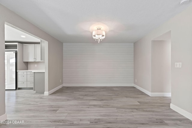 unfurnished dining area featuring light hardwood / wood-style flooring, wood walls, a textured ceiling, and an inviting chandelier