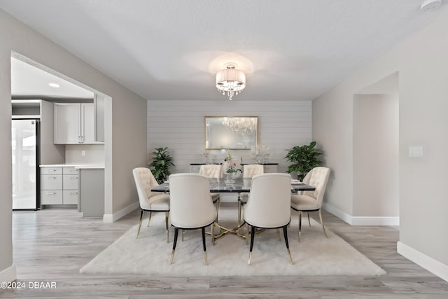 dining room featuring wood walls, a textured ceiling, a notable chandelier, and light hardwood / wood-style flooring