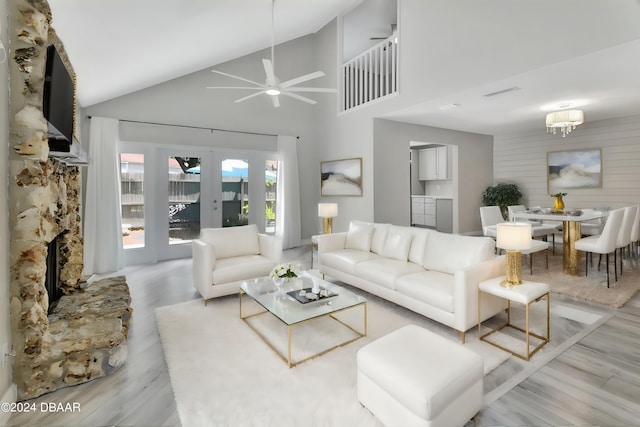 living room with a stone fireplace, ceiling fan with notable chandelier, light hardwood / wood-style flooring, and high vaulted ceiling