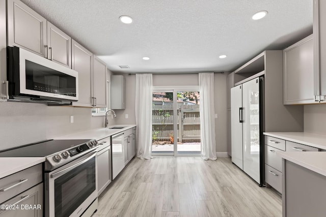 kitchen featuring stainless steel appliances, light hardwood / wood-style floors, sink, a textured ceiling, and gray cabinetry