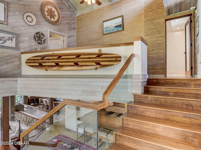 stairway with a towering ceiling, wood walls, and ceiling fan