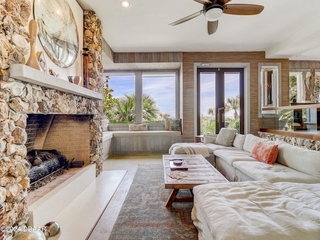 living room featuring a stone fireplace, concrete floors, and ceiling fan