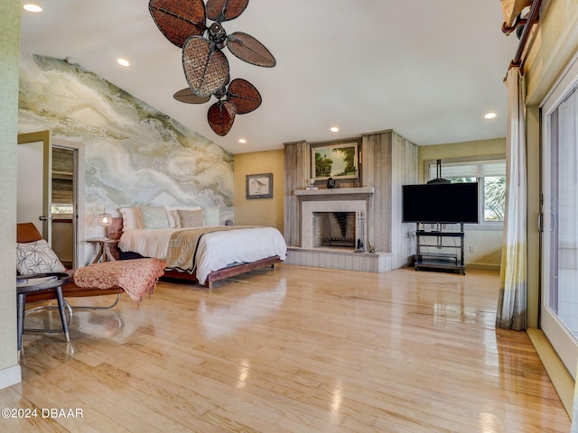 bedroom featuring ceiling fan, a tiled fireplace, and light hardwood / wood-style floors