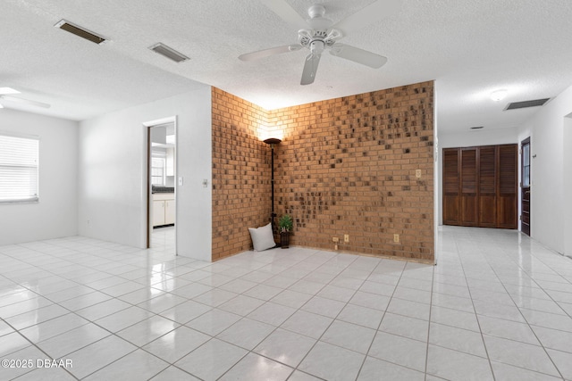 tiled spare room featuring a textured ceiling, ceiling fan, and brick wall