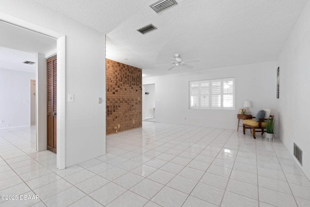 unfurnished living room featuring ceiling fan, light tile patterned floors, a textured ceiling, and brick wall