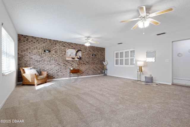 unfurnished living room featuring ceiling fan, light colored carpet, brick wall, and a textured ceiling