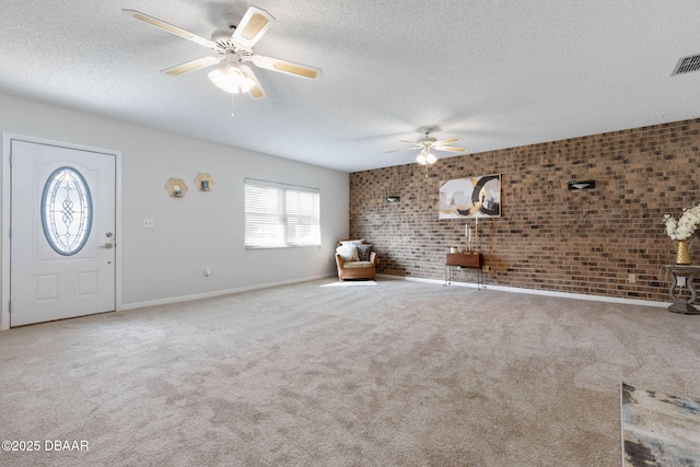 unfurnished living room featuring ceiling fan, carpet floors, a textured ceiling, and brick wall