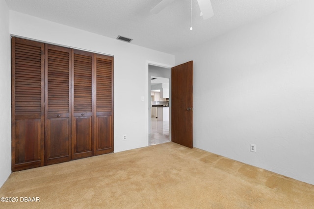 unfurnished bedroom featuring light carpet, a textured ceiling, a closet, and ceiling fan