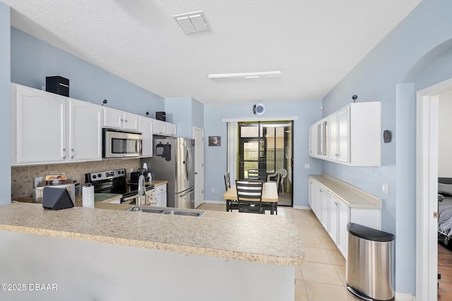 kitchen featuring kitchen peninsula, appliances with stainless steel finishes, light tile patterned floors, and white cabinetry