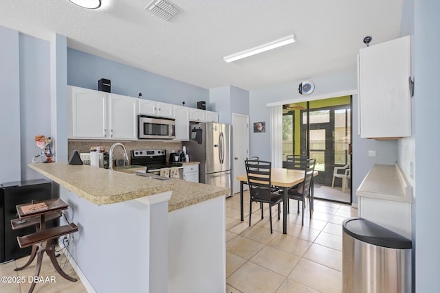 kitchen featuring kitchen peninsula, a textured ceiling, stainless steel appliances, light tile patterned floors, and white cabinetry