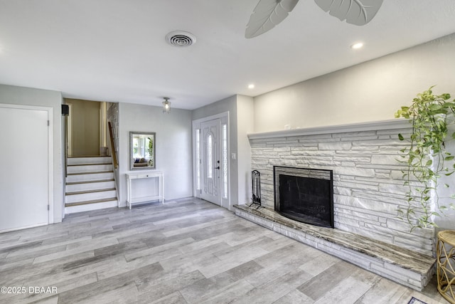 unfurnished living room with wood finished floors, visible vents, a fireplace, recessed lighting, and stairs