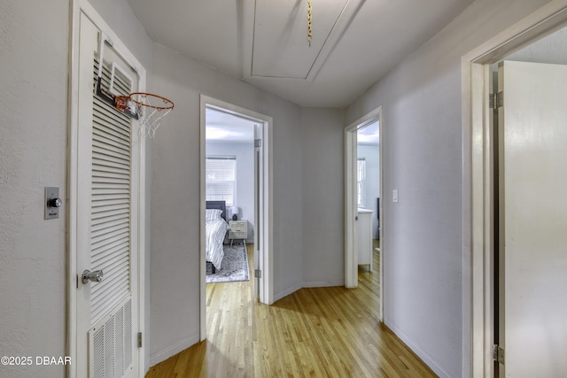 hall featuring light wood-type flooring, baseboards, attic access, and visible vents