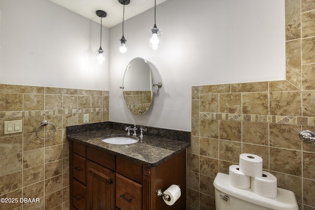 half bath with vanity, tile walls, toilet, and a wainscoted wall