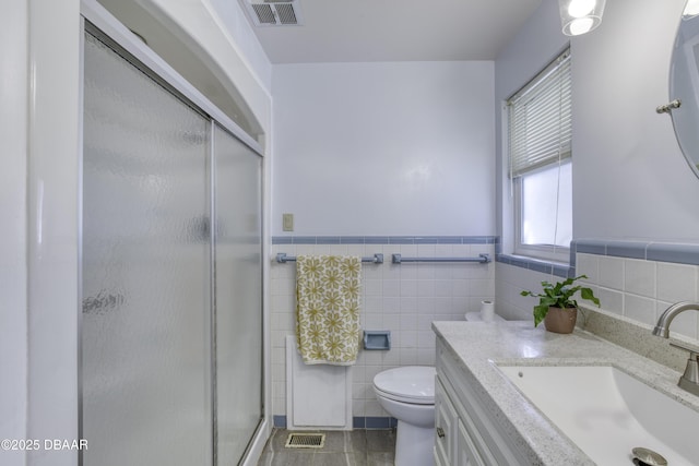 bathroom with visible vents, toilet, tile walls, and a stall shower