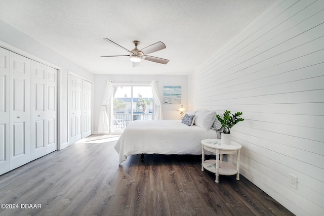 bedroom with a textured ceiling, dark hardwood / wood-style floors, access to exterior, wooden walls, and ceiling fan