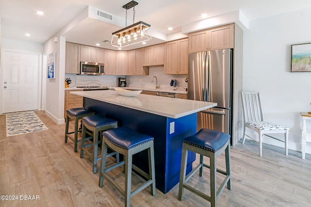 kitchen with stainless steel appliances, light brown cabinetry, decorative light fixtures, a kitchen island, and light wood-type flooring