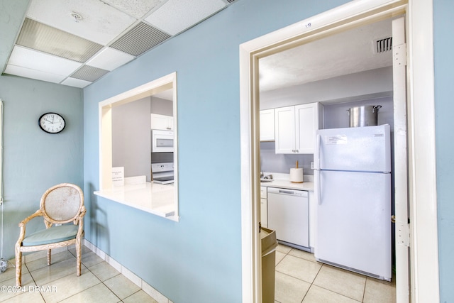 kitchen featuring light tile patterned floors, white appliances, white cabinetry, and a paneled ceiling