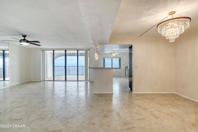 empty room with ceiling fan with notable chandelier, expansive windows, and a textured ceiling