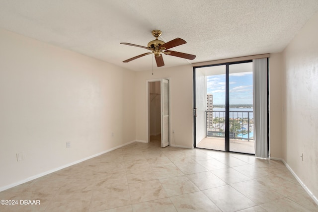 unfurnished room featuring expansive windows, a textured ceiling, ceiling fan, light tile patterned floors, and a water view