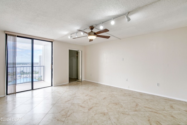 spare room with a textured ceiling, expansive windows, ceiling fan, and rail lighting