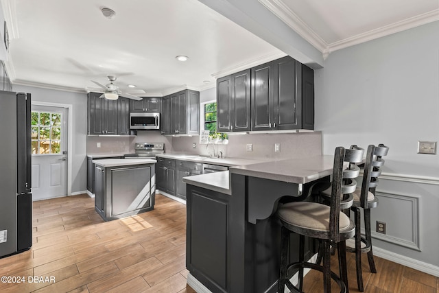 kitchen with a kitchen bar, kitchen peninsula, ceiling fan, light wood-type flooring, and appliances with stainless steel finishes