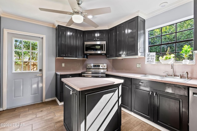 kitchen with stainless steel appliances, sink, ornamental molding, a kitchen island, and light wood-type flooring