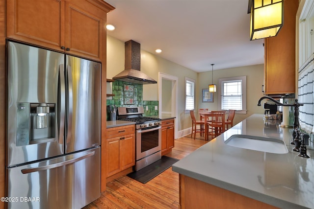 kitchen featuring tasteful backsplash, extractor fan, light wood-style flooring, appliances with stainless steel finishes, and a sink