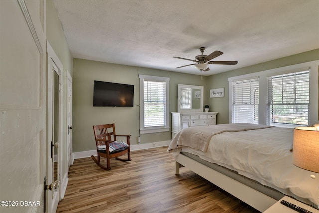 bedroom with a ceiling fan, wood finished floors, baseboards, and a textured ceiling