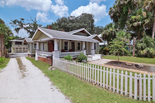 view of front of home with a fenced front yard, a porch, a front yard, a chimney, and driveway