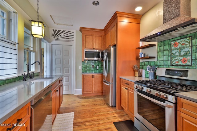 kitchen featuring light wood-style flooring, brown cabinets, appliances with stainless steel finishes, wall chimney exhaust hood, and a sink