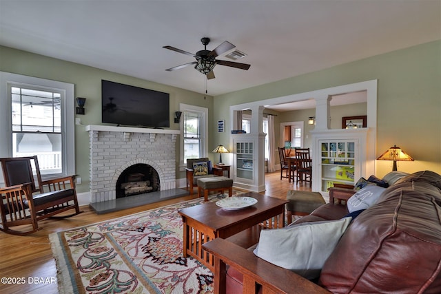 living area with visible vents, wood finished floors, a fireplace, ceiling fan, and ornate columns