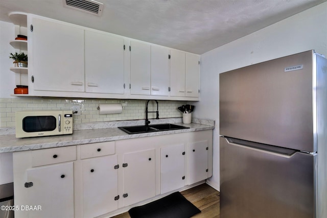 kitchen featuring white microwave, visible vents, open shelves, freestanding refrigerator, and a sink